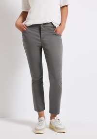 Pantalons gris ajustés en mélange de coton, avec poches avant, texture lisse et longueur cropped, associés à des baskets blanches.