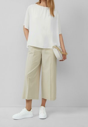 Witte, losvallende blouse met een ronde hals, gecombineerd met beige, wijde broekspijpen en witte sneakers. Eenvoudig en strak ontwerp.