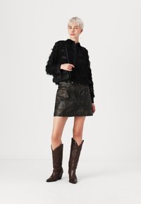 Giacca nera di piume, mini gonna in pelle scura con tasche e stivali da cowboy marroni con punta appuntita e motivi intricati.
