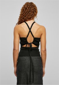 Černý žebrovaný halter top s překříženými ramínky, odhaleným zadním dílem a nastavitelným vázáním, spárovaný s tmavými denimovými sukněmi s kapsami.