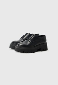 Chaussures en cuir noir avec un bout arrondi, présentant une semelle épaisse crantée et six paires d'œillets pour les lacets. Texture lisse.