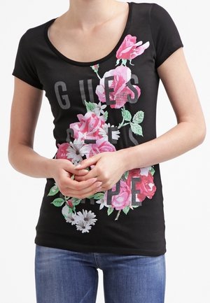 Sort t-shirt med korte ærmer og blomsterprint i pink og hvid, med teksten "GUES" i store bogstaver. Blødt, strækbart bomuldsmateriale.