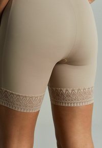 Beige tvarovací šortky s jemnou, hladkou texturou a složitou krajkovou dekorací na lemu, s diamantovým vzorem v světlejší béžové.