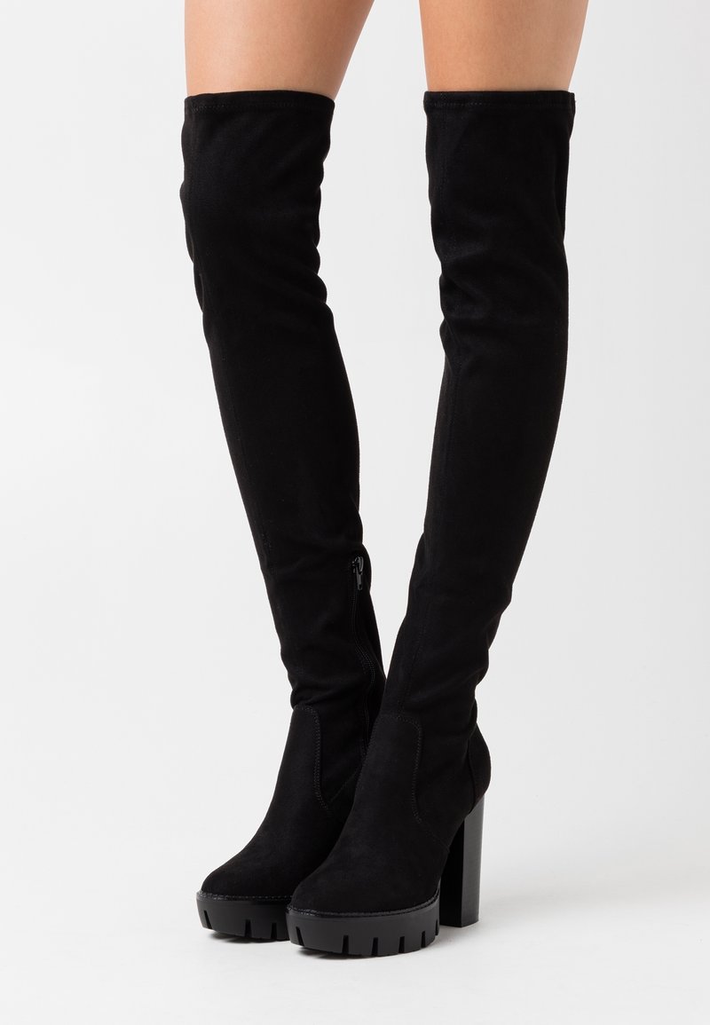 Bottes cuissardes en daim noir avec un talon épais et une finition texturée, dotées d'une fermeture éclair latérale pour un enfilage facile. Design lisse et élégant.