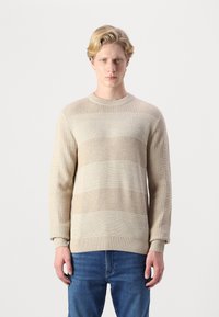Maglione lavorato a maglia beige con righe orizzontali in diverse trame, polsini a coste e scollatura rotonda, abbinato a jeans blu.