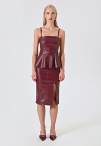 Burgunderfarbenes, täuschend echtes Leder Peplum-Top und Bleistiftrock-Set mit verstellbaren Trägern, seitlichem Schlitz und glatter Textur; getragen mit passenden spitzen Absätzen.