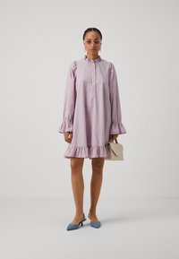 Rosa stripete, kneelengde kjole med rynkede mansjetter og kant. Båret med blå slingback hæler og holdt en lys beige håndveske.