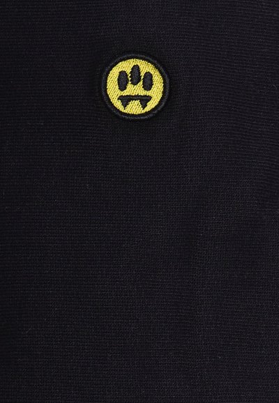 Tessuto nero con un sorriso ricamato giallo che fa una smorfia, che mostra una forma rotonda con tre punti e due forme a triangolo per la bocca.