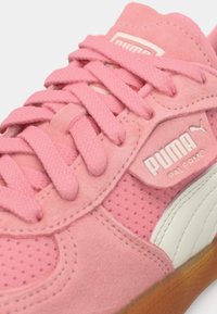 Gros plan sur une basket Puma Palermo rose montrant les lacets, la texture en daim, le tissu perforé, la bande blanche Puma et la semelle en gomme.