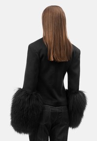 Giacca nera aderente con morbidi accenti di pelliccia nera ai polsini, con una texture elegante e una silhouette dritta.