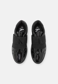 Black patent leather sneakers with a rounded toe, wide elastic band featuring a logo, and padded ankle for comfort.