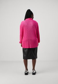 Top de manga larga fucsia con textura acanalada, utilizado sobre una falda lápiz de cuero negra y zapatos de plataforma plateados.