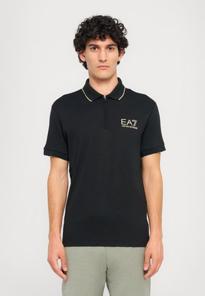 Black polo shirt with a zip collar, gold accents, and EA7 logo on the left chest. Short sleeves with matching cuff trim. Smooth fabric texture.