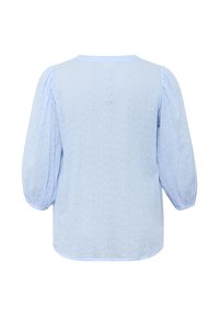 Blouse bleu clair avec des manches bouffantes, présentant un motif texturé et un col rond. Le tissu semble léger et aérien.
