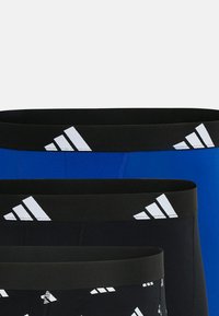 Tre par idrottsshorts: ett par i helblått, två svarta med vita mönster, med svarta elastiska midjeband med vita logodetaljer.