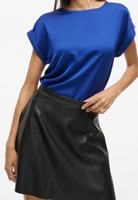 Haut bleu en satin à manches courtes avec un col rond, associé à une jupe en cuir noire avec une taille cintrée et un plissage discret.