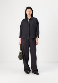 Dark linen button-up shirt with rolled sleeves, paired with loose-fitting dark trousers. Accessory: small olive green bag.