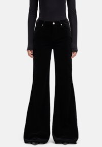 Pantaloni a zampa in velluto a coste nero con design a cinque tasche, cuciture visibili e ferramenta in metallo grigio. Tessuto morbido e apertura gamba ampia.