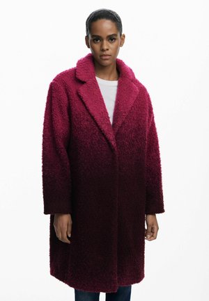 Fluffy kastanjebruine jas met een notch-kraag, zichtbare knopenrij en grote zakken. Gelaagd textiel met een gradient-effect naar donkerdere tinten.