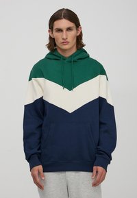 Hoodie w kolorze zielonym, białym i granatowym w wzór chevron. Wykonany z miękkiego materiału, posiada przednią kieszeń i regulowany sznurek.