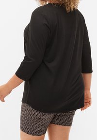 Mustat lyhyet hihatopit, joissa on rento istuvuus, yhdistettynä kuvioituihin mustiin shortseihin, joissa on geometrinen muotoilu. Pehmeä materiaali, sileä pinta.