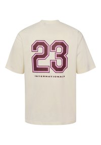 Flødefarvet bomulds-t-shirt med et stort vinrødt "23" med lyserøde accenter og ordet "INTERNATIONALS" nedenunder i sort. Korte ærmer og løs pasform.