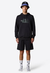 Black hoodie with a front pocket and "The North Face" logo, paired with black shorts and white socks featuring repeated logo print. Black bucket hat.