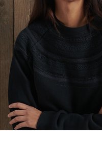 Sudadera negra con tejido texturizado, cuello redondo y patrones decorativos en la parte superior del cuerpo. Material suave y acogedor.
