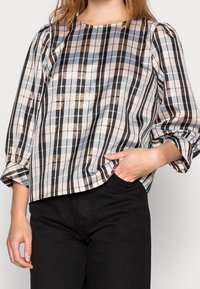 Vaalean ruudullinen paita, jossa on puffihihat ja sinisiä, mustia ja pronssinvärisiä raitoja vaaleaa taustaa vasten. Sileä kangas ja pyöreä pääntie.