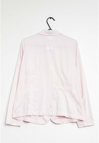 Light pink long-sleeve shirt with a collared neck, featuring thin vertical stripes and a curved hem. Displayed hanging on a black hook.