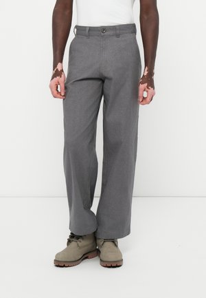 Graue Hose aus strukturiertem Stoff, mit Knopfverschluss, Gürtelschlaufen und weitem Bein, kombiniert mit grauen Schnürstiefeln.