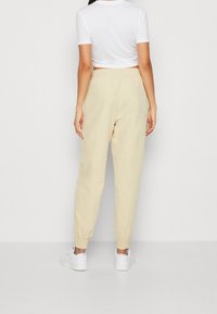 Beige jogger pants with an elastic waistband and cuffs, made from a smooth fabric, paired with white sneakers. Plain design, no visible pattern.