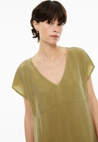 Leichtes Kleid in Olivgrün mit V-Ausschnitt, kurzen Ärmeln und einem lockeren Schnitt. Verfügt über subtile Nahtdetails und eine glatte Textur.