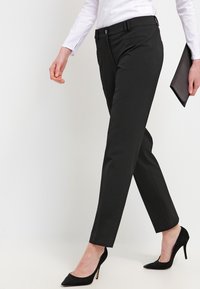 Pantalons noirs ajustés en tissu lisse, présentant une coupe slim, des passants de ceinture, des poches latérales et assortis à des talons hauts noirs.