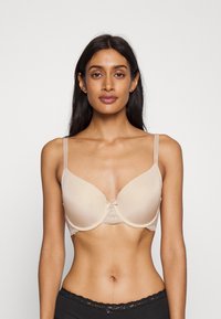 Beige padded bra with lace trim, soft fabric, adjustable straps, and a small bow detail at the center. Smooth, contour shape.