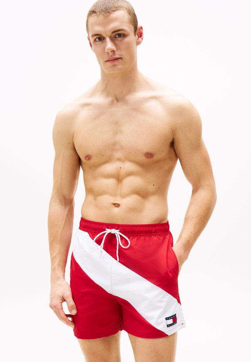 Shorts de bain rouges avec une bande blanche diagonale, taille élastique à cordon, et patch logo. Fabriqués en tissu léger, adaptés aux activités aquatiques.
