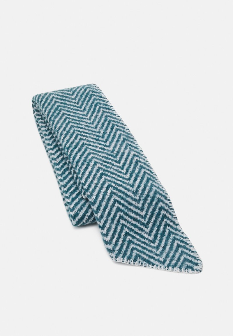 Écharpe bleu sarcelle présentant un motif en chevrons blanc. En tissu doux, elle a une forme effilée avec une finition nette et bordée.