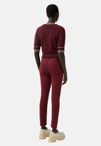 Burgundy knit sweater with contrasting white stripes on sleeves paired with fitted burgundy pants. Model wears chunky beige platform shoes.