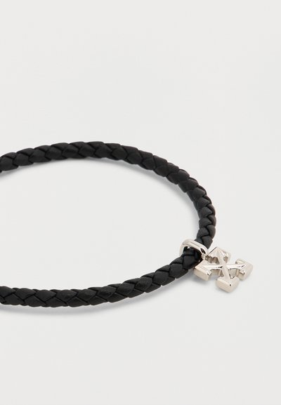 Bracelet en cuir noir tressé avec un petit pendentif métallique argenté en forme de croix attaché.