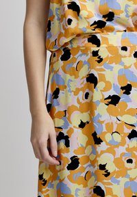 Rochie florală în nuanțe de portocaliu, galben și albastru, cu accente negre. Material moale, design fluid, cu modele mari de flori abstracte.