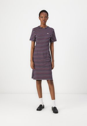 Gestreiftes Kleid in Marineblau, Rot und Weiß; kurze Ärmel; Rundhalsausschnitt; knielange Passform mit subtilen Seitenschlitzen; getragen mit schwarzen Slippern und weißen Socken.