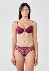 Completo di lingerie in pizzo bordeaux con reggiseno balconcino dai bordi ondulati e slip in rete trasparente decorati con motivi floreali.