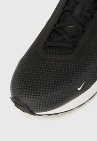 Mustad spordijalats võrguga pealiskihil, millel on täplik mustriga, tekstuurse küljele, valge kontrastse logoga ja sileda valge tallaga.