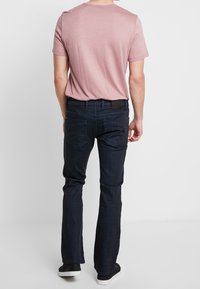 Camiseta de hombre en rosa claro y jeans azul oscuro con corte recto. Los jeans cuentan con bolsillos traseros con detalles de costura y una cinturilla negra.