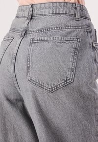 Vaqueros de denim gris con un corte holgado, cinturilla estructurada y dos bolsillos traseros con detalles de costura minimalistas. Tejido texturizado.