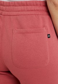 Roze katoenen joggers met een elastische tailleband, voorzien van een achterzak en een klein logo-label. Gladde textuur met gestikte details.