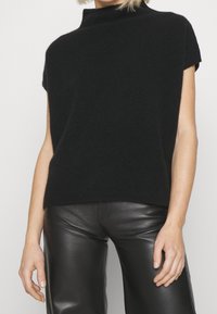 Jersey negro de manga corta con un alto cuello, hecho de un material suave. Presenta un corte recto y un dobladillo acanalado, combinado con pantalones de cuero negro brillantes.