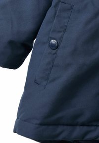 Jūras spēku zila jaka ar pogu aizdari uz kabatas. Audums izskatās gluds ar nelielu spīdumu un salocītu piedurkņu detaļu.