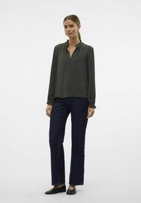 Donkergroen blouse met een gerimpelde halslijn, lange mouwen en een ontspannen fit, gecombineerd met donkerdenim rechte broek en zwarte platte schoenen.