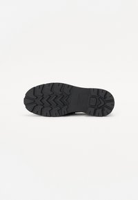 Suela de zapato de goma negra con profundas ranuras y patrones en zigzag para tracción; puntera plana y redondeada; acabado liso y texturizado; sin marcas visibles.